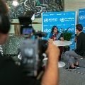 A cameraman shooting two people against WHO-branded backdrop