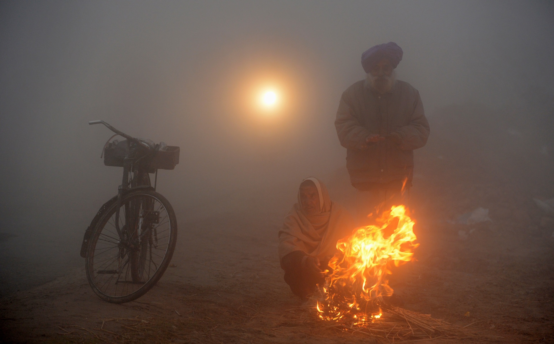 Indian farmers warm themselves around a fire facing air pollution