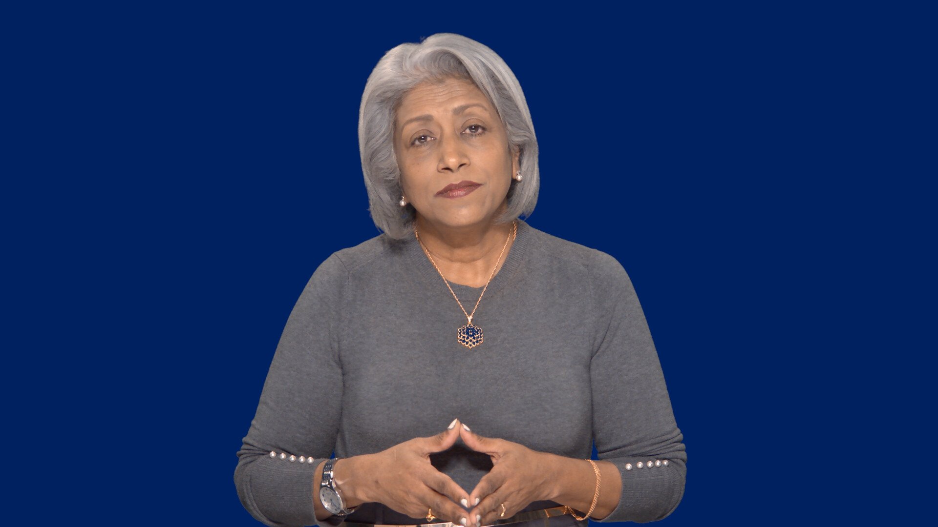 A woman in front of a dark blue background looking into the camera.