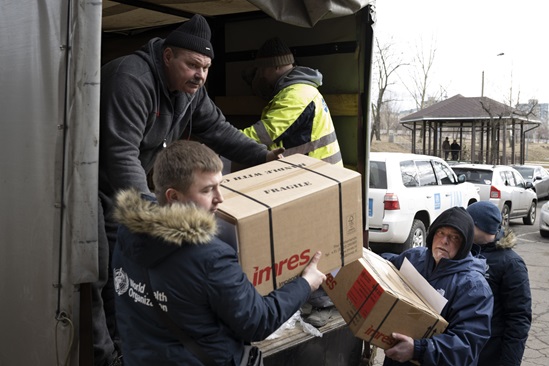 Five men, one wearing a WHO jacket emptying cartons from the back of a truck.