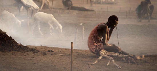 A man is sitting on the very dry ground with animals faded in the background.