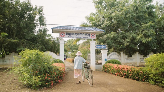 A woman wheels her bike to a health centre in Cambodia.