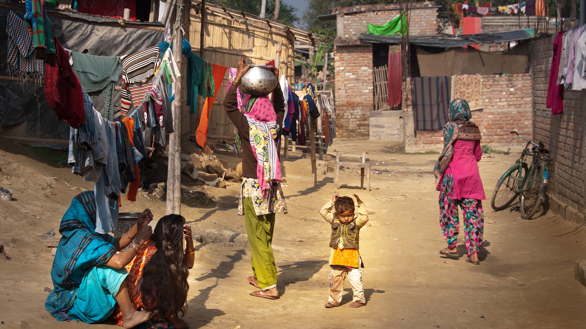 Photo of people walking and sitting on a dirt road between homes in Darbhanga, India.