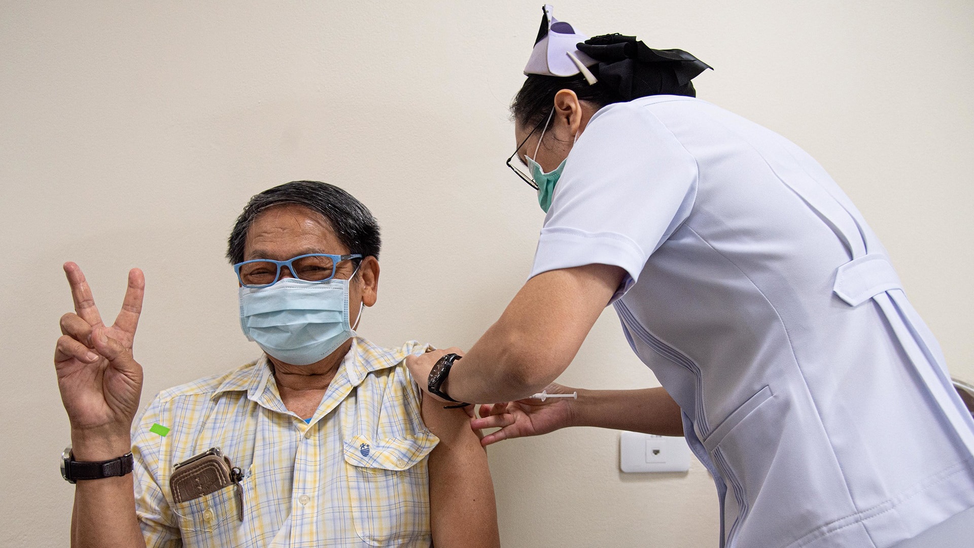 Photo of a male patient wearing a mask being vaccinated by a medical worker in a Bangkok hospital.