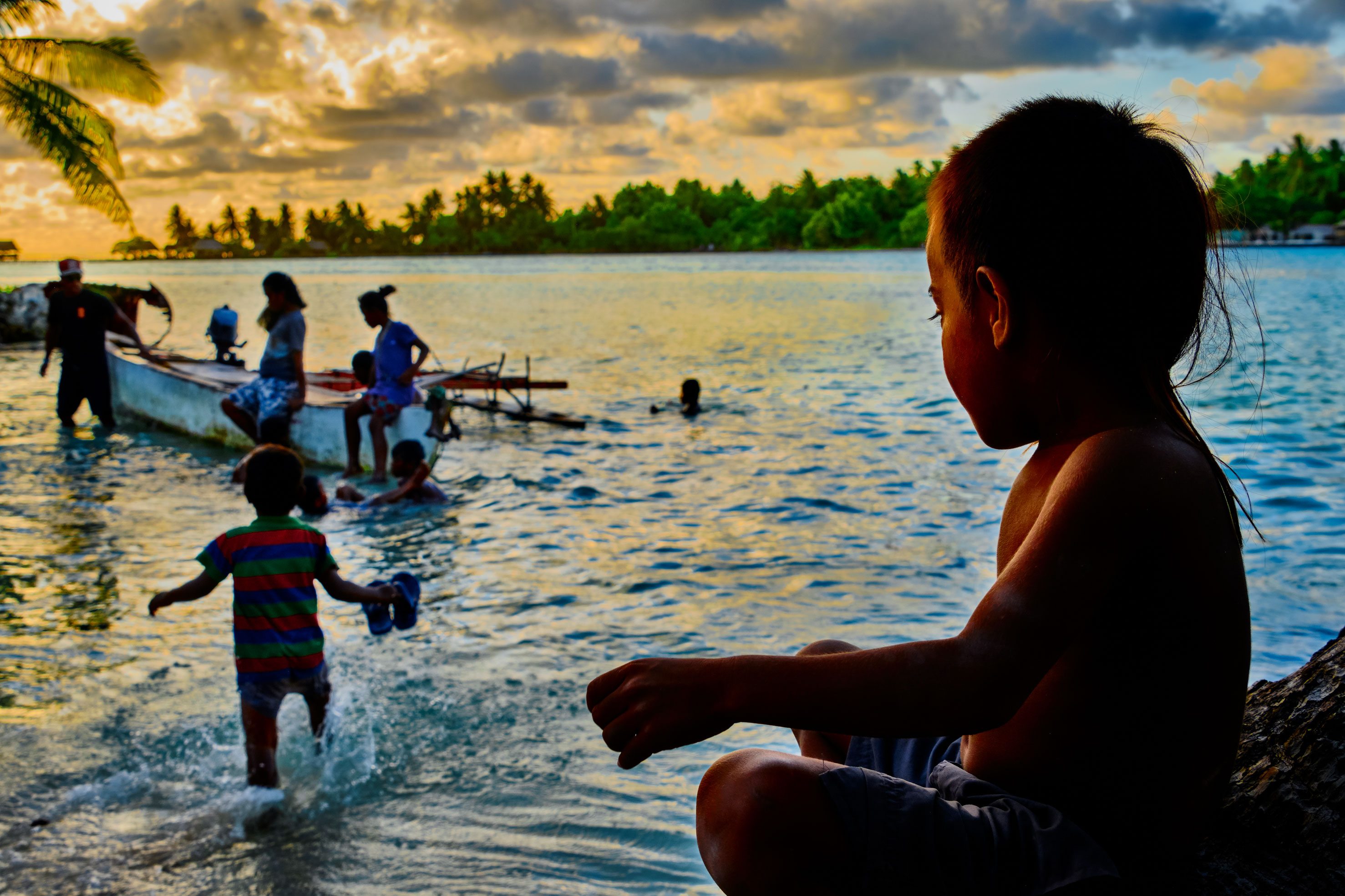 Des enfants jouent dans l'eau à la tombée de la nuit.