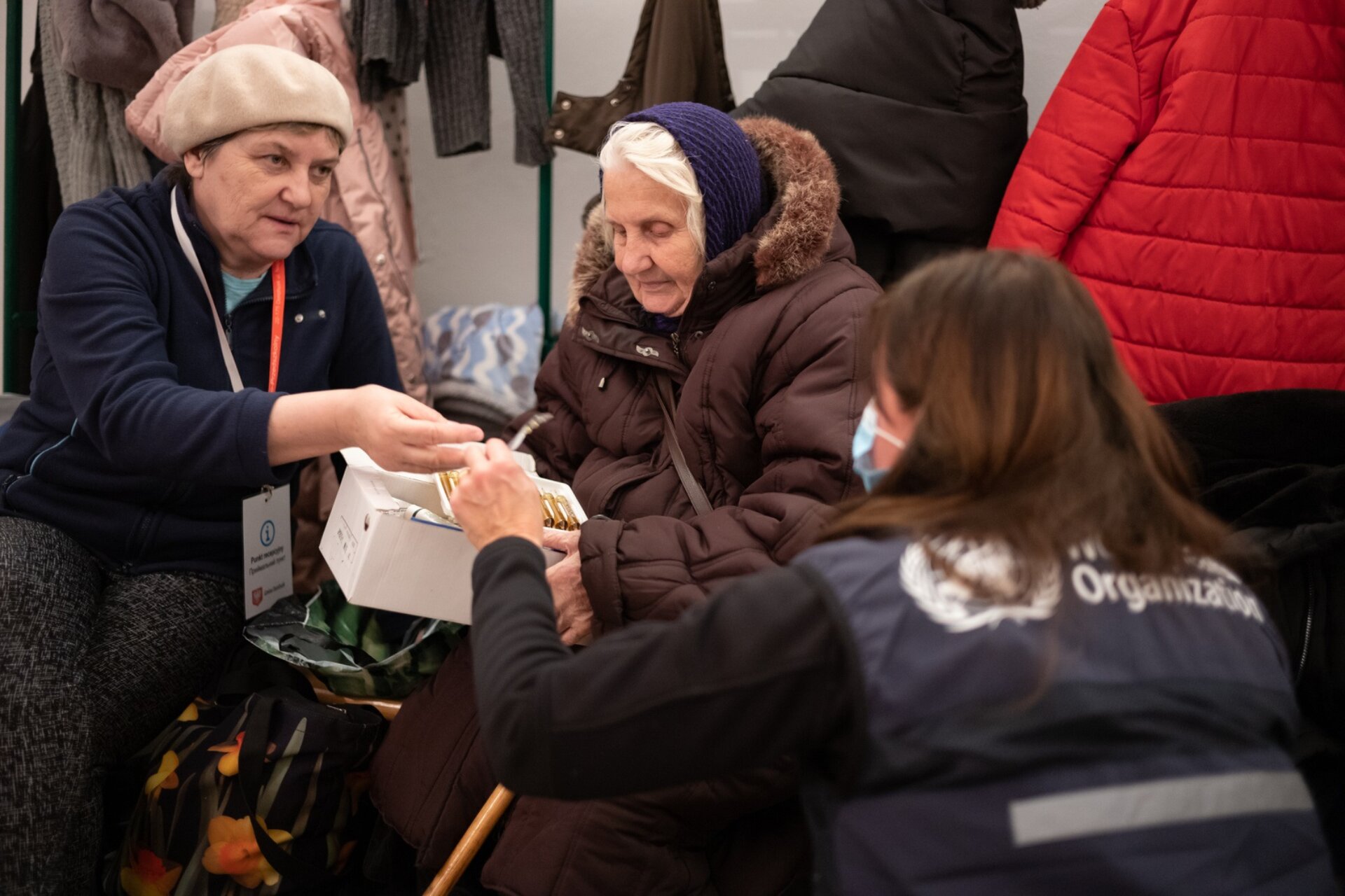 A nurse and a WHO Officer is attending to an elderly woman, dressed in a warm winter coat.