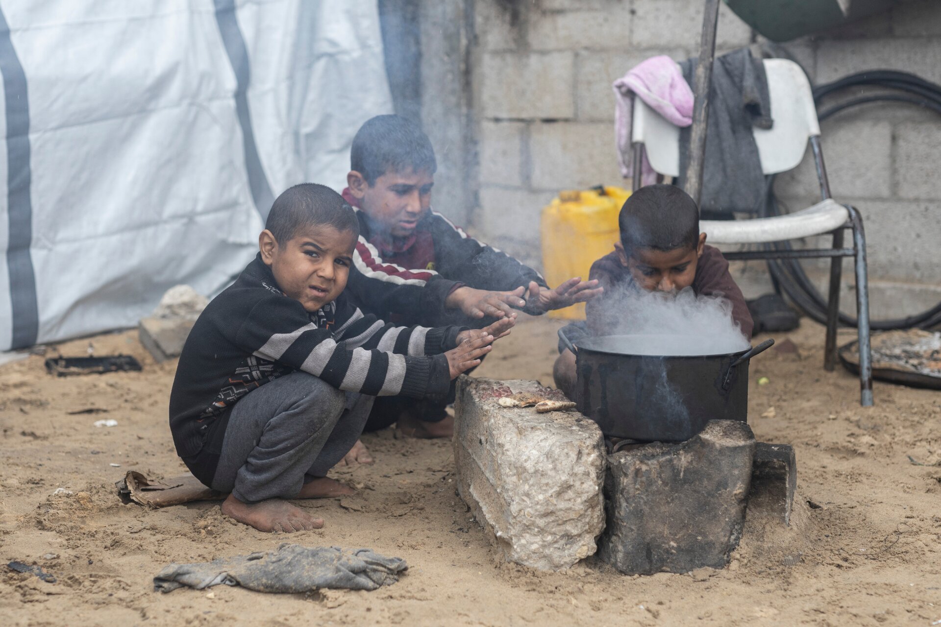 Gazan boys in a displacement camp Young boys without shoes warming their hands over a saucepan.