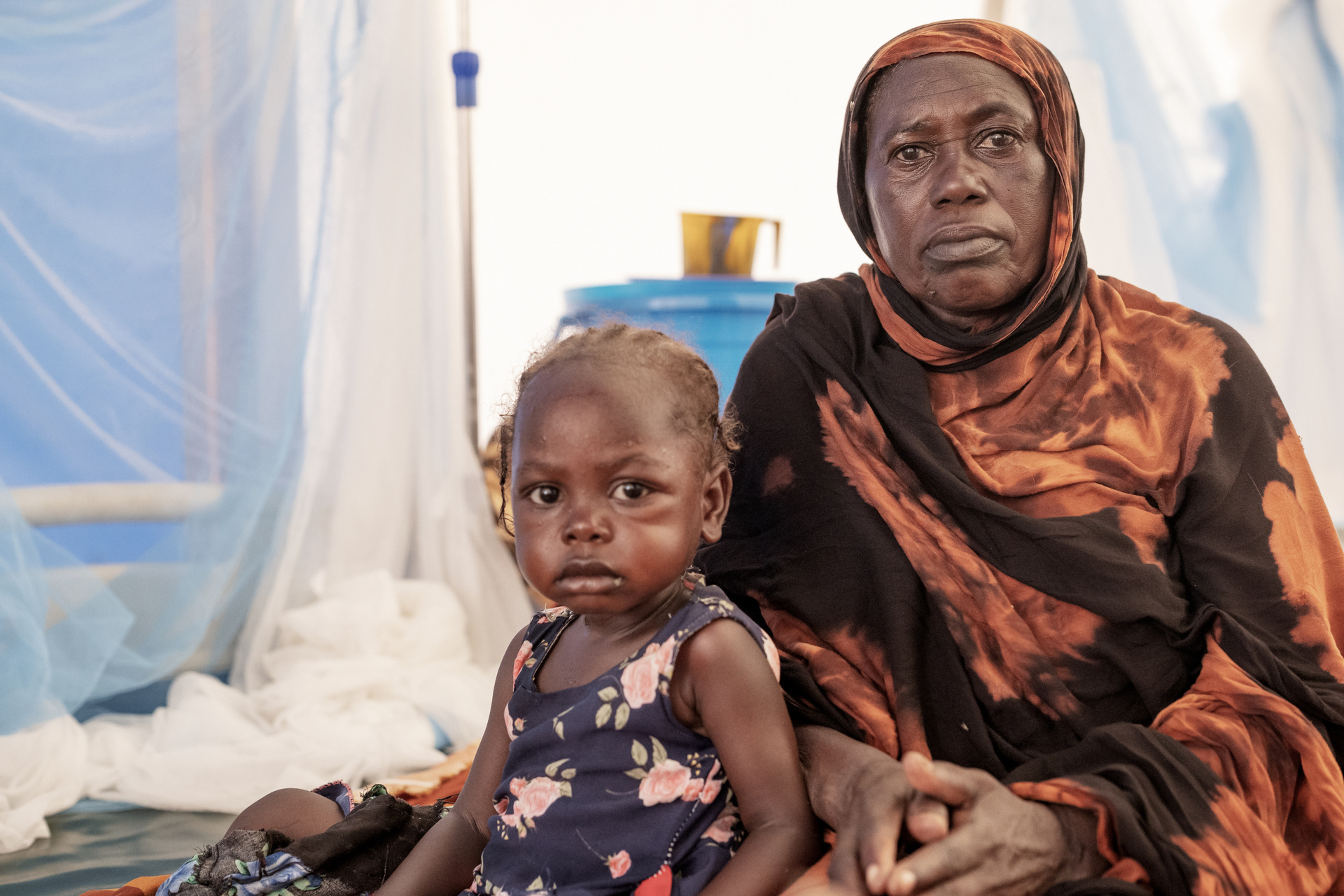 A woman and a young child sitting in a tent with serious expressions