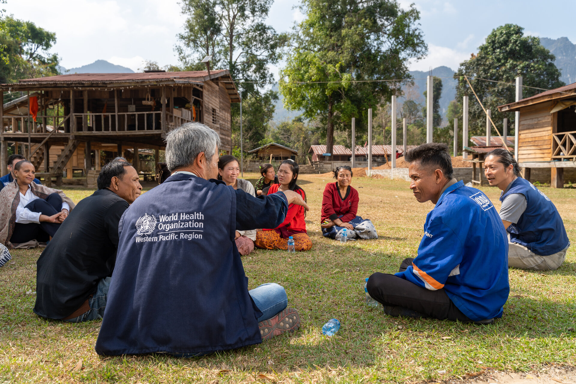 Staff and community health workers sitting down in a field to discuss health priorities