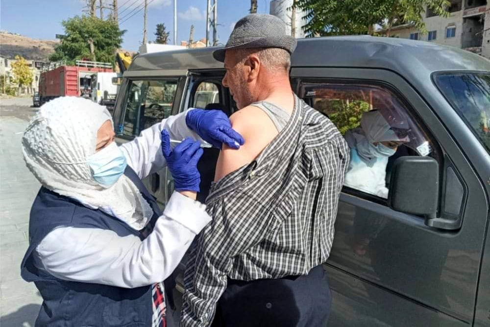 A female health worker is giving a vaccine shot to a man in the street of a rural village