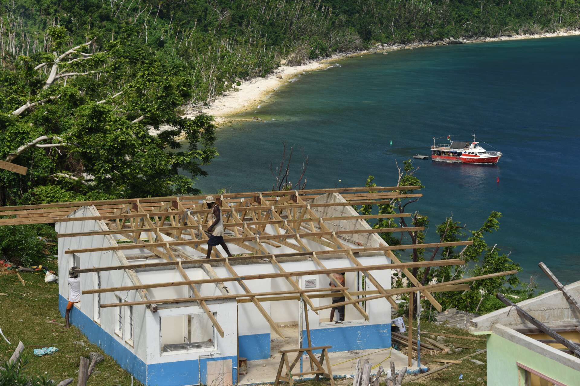 People working to build a new roof on a house, on a hill next to the sea