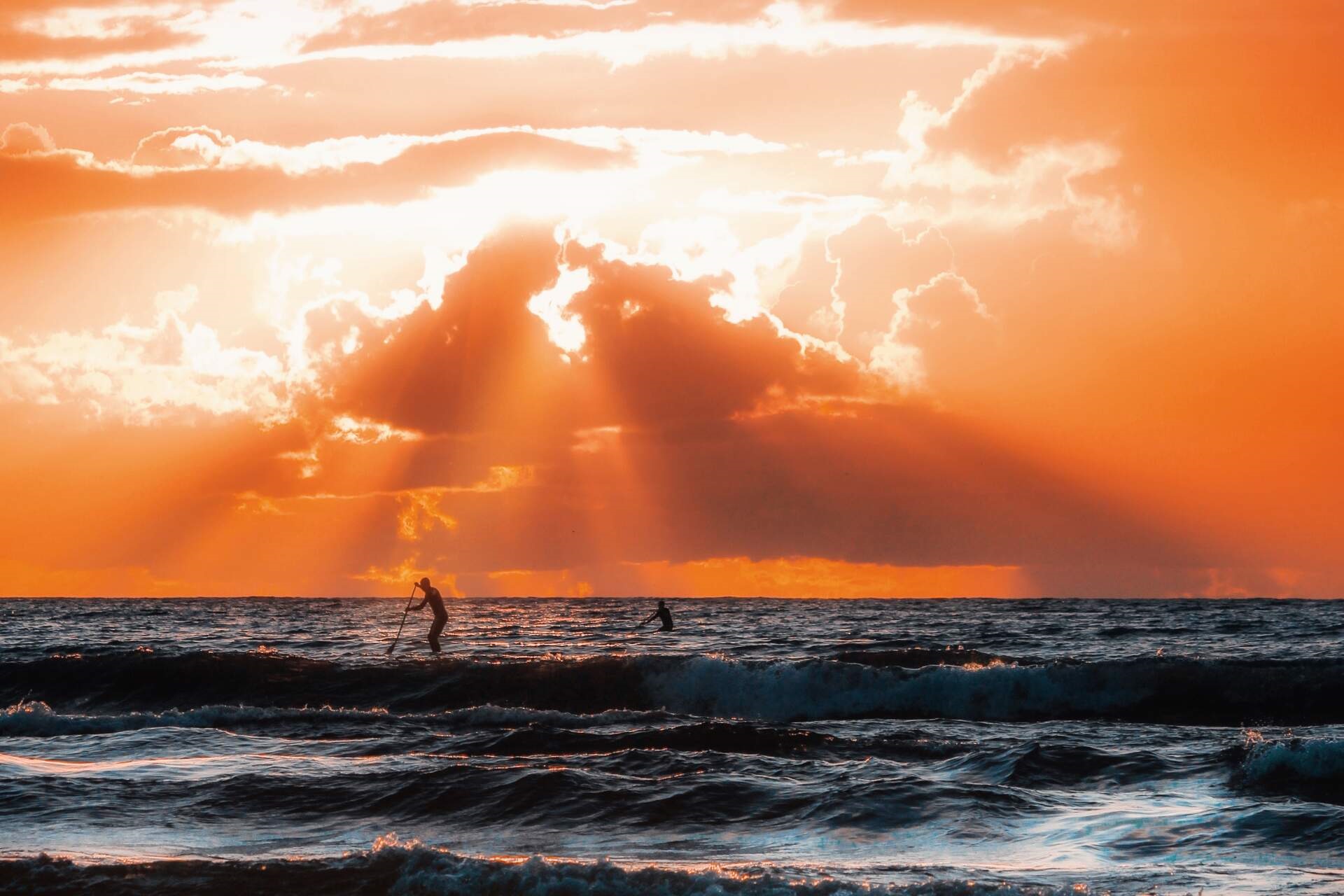 Watersport in sunset Estonia The silhouette of two paddleboarders seen at sea under a powerful red sunset