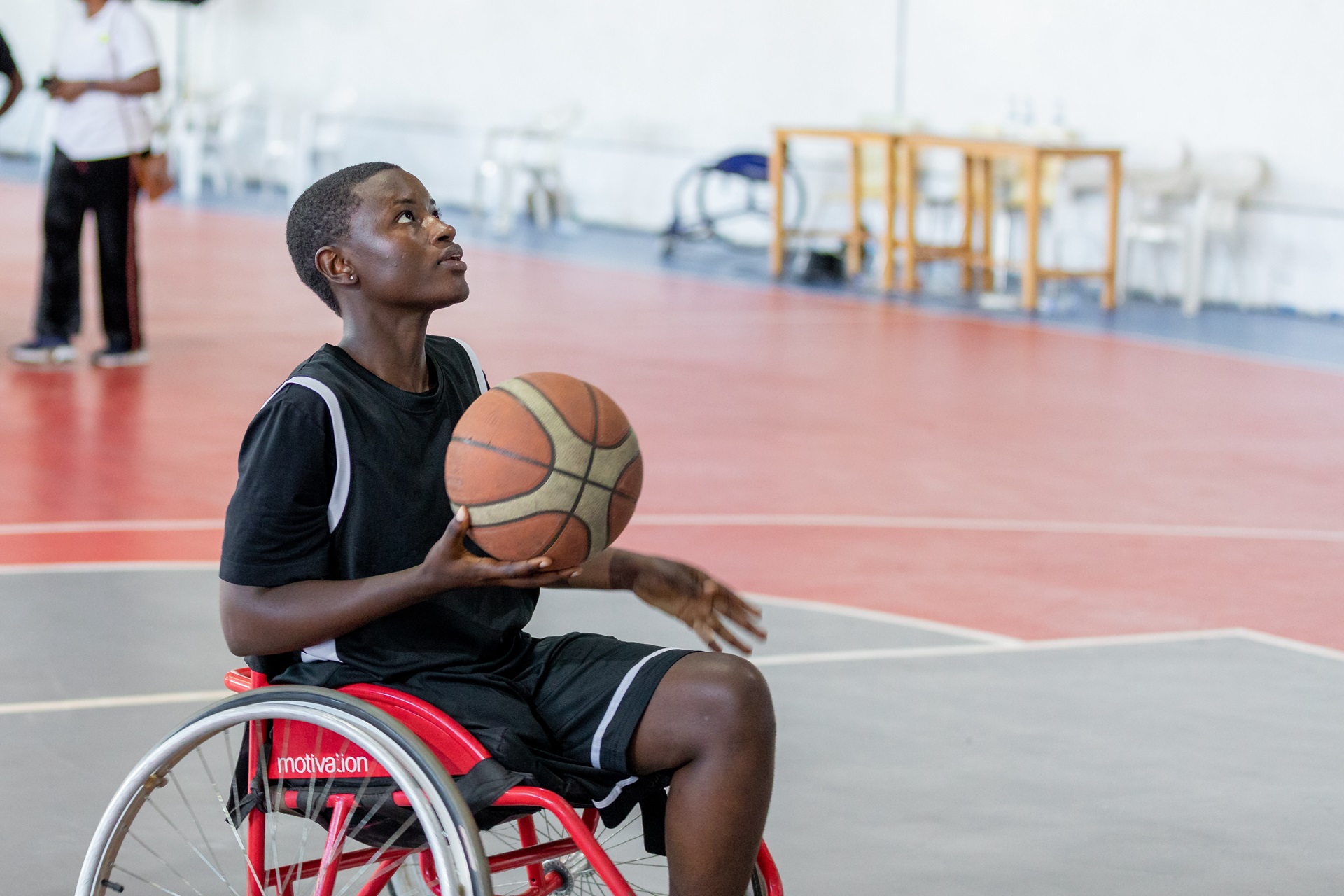 Gavi Rwanda Woman basketball player with disability A woman basketball player in Rwanda, holding a basketball in her right hand, sitting in a wheelchair, to aim towards hoop