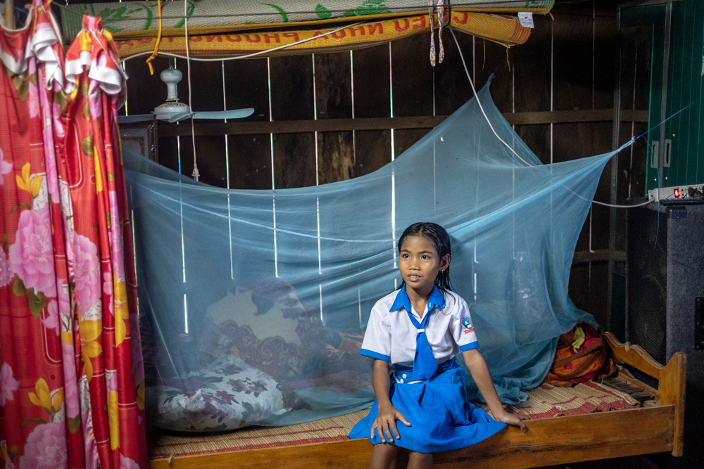 Girl sits next to a bed net in her house