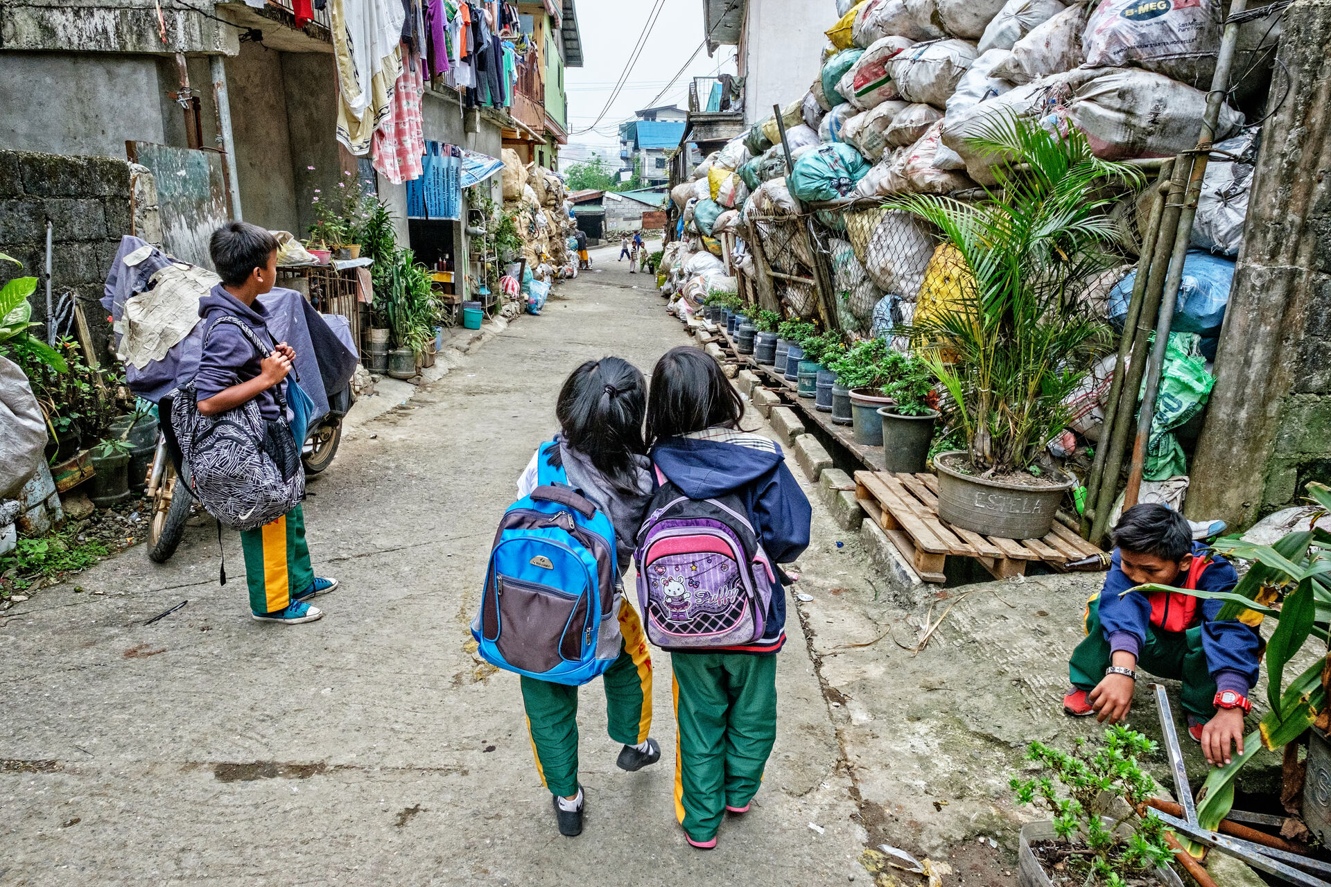 Two girls and boys walking in a street which has several packages of plastic waste.