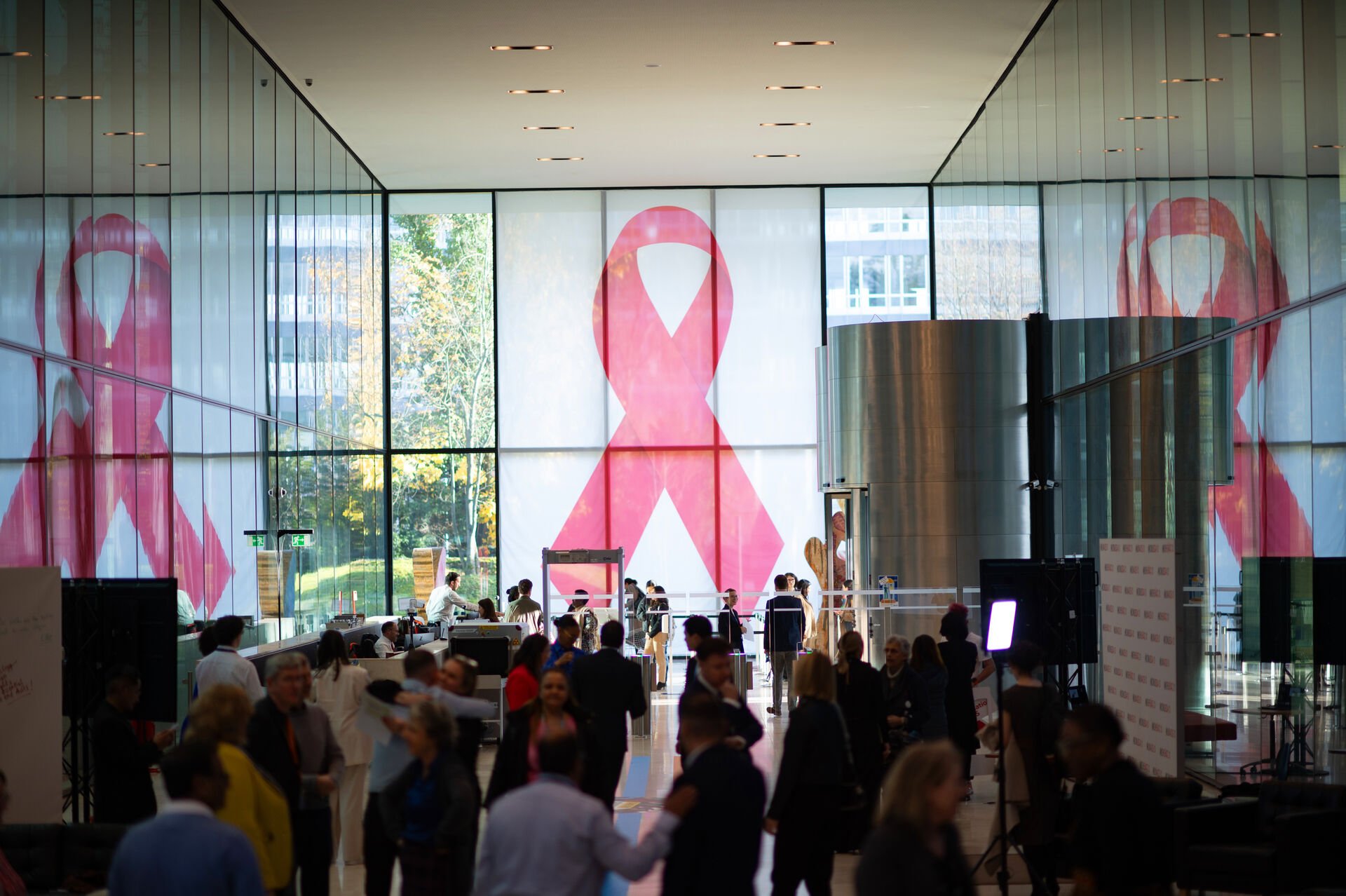 A large group of people gathering in a spacious lobby, with a giant red ribbon on the window front.