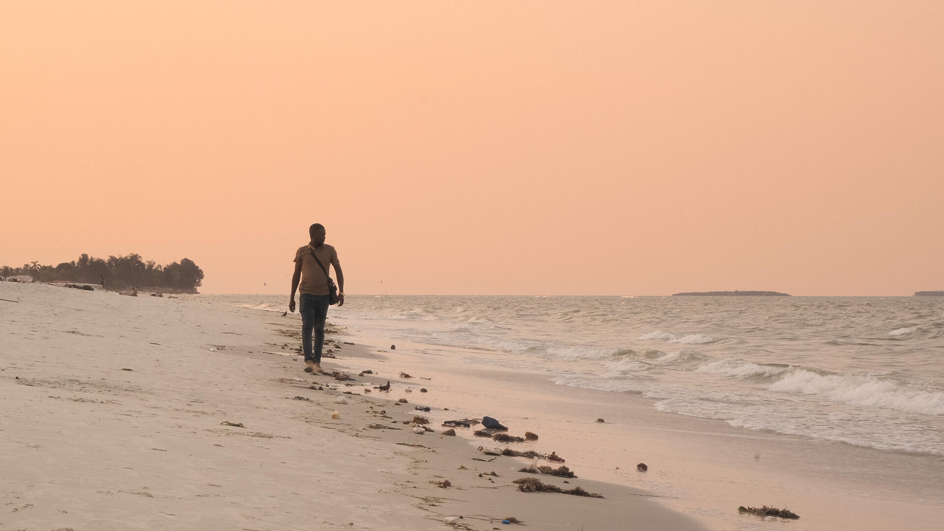A man walks on the beach, with a colorful sunset casting shadows around him.