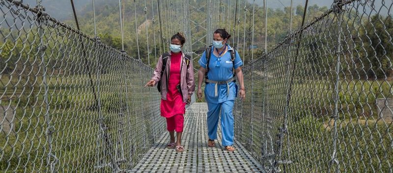 Two women walk across a suspension bridge side by side.