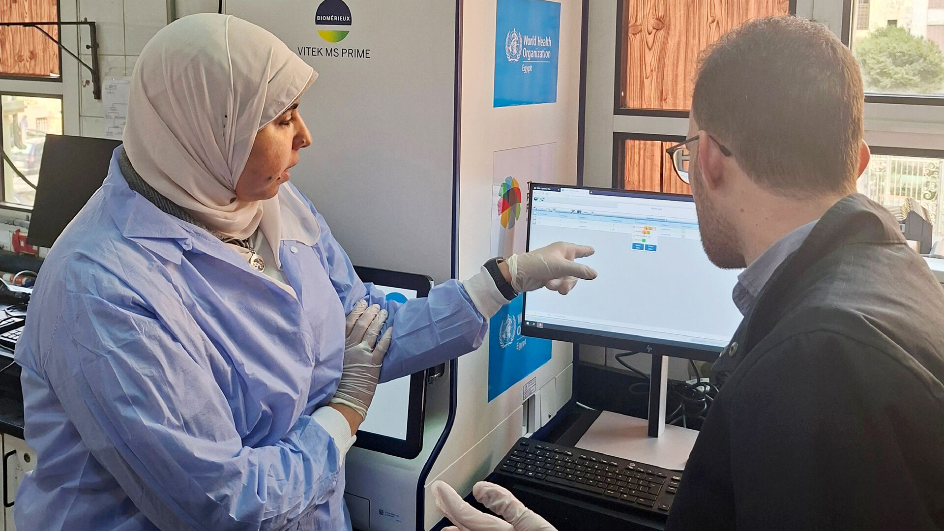 A health worker wearing protective gear stidies data on computer with another colleague, in Egypt