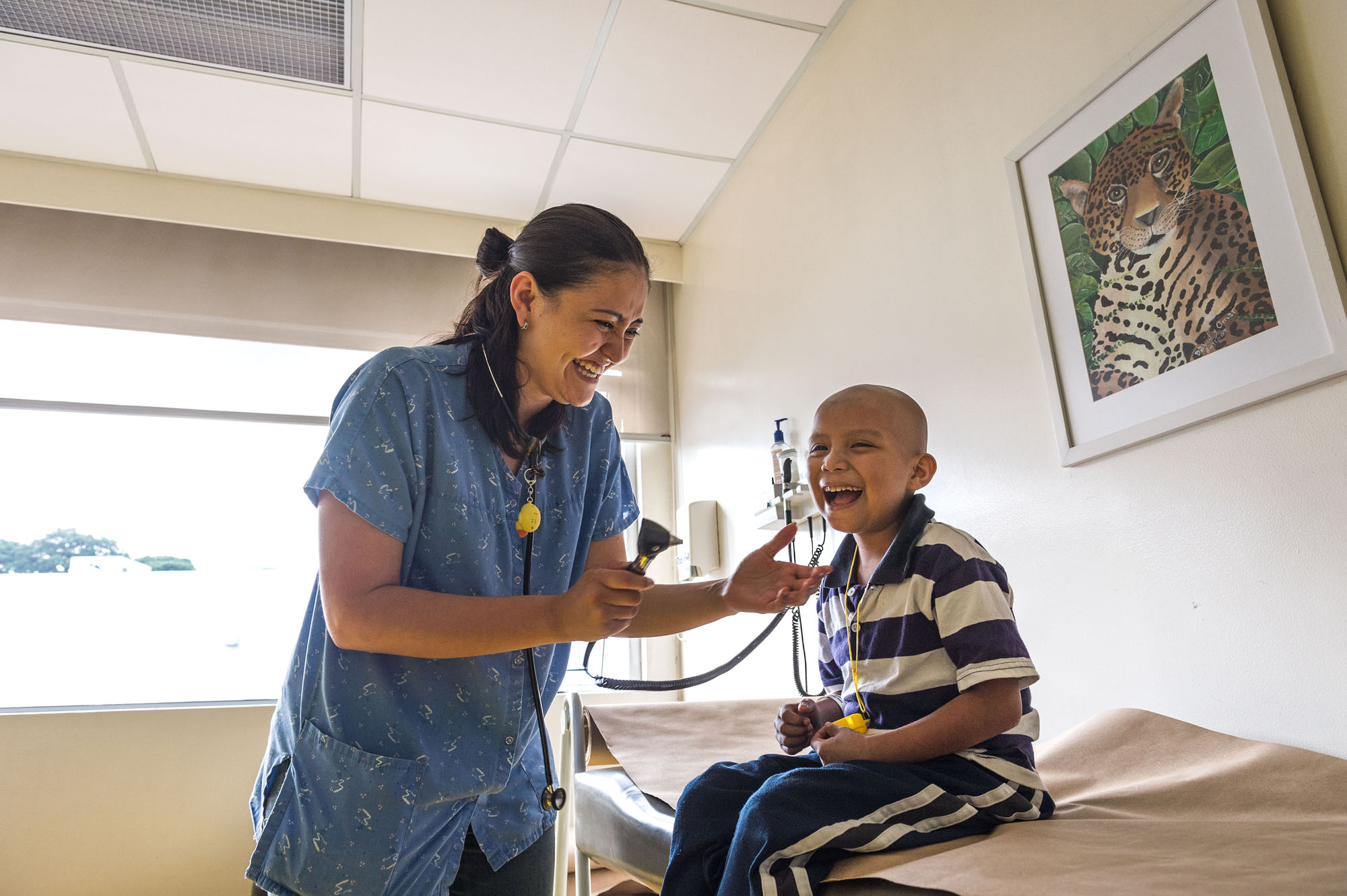 Global childhood cancer initiative hero image A female health care worker is examining a smiling happpy boy who's sitting on a hospital bed.
