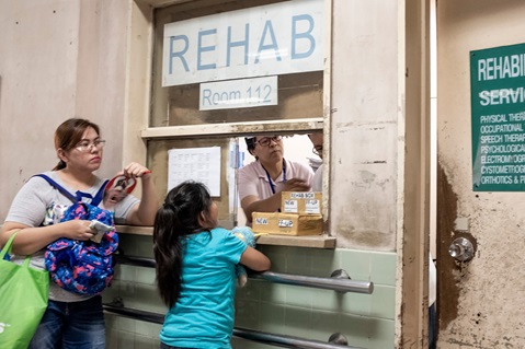 A woman and young girl looking through a serving hatch at a rehab services 2 people are on the other side of the window