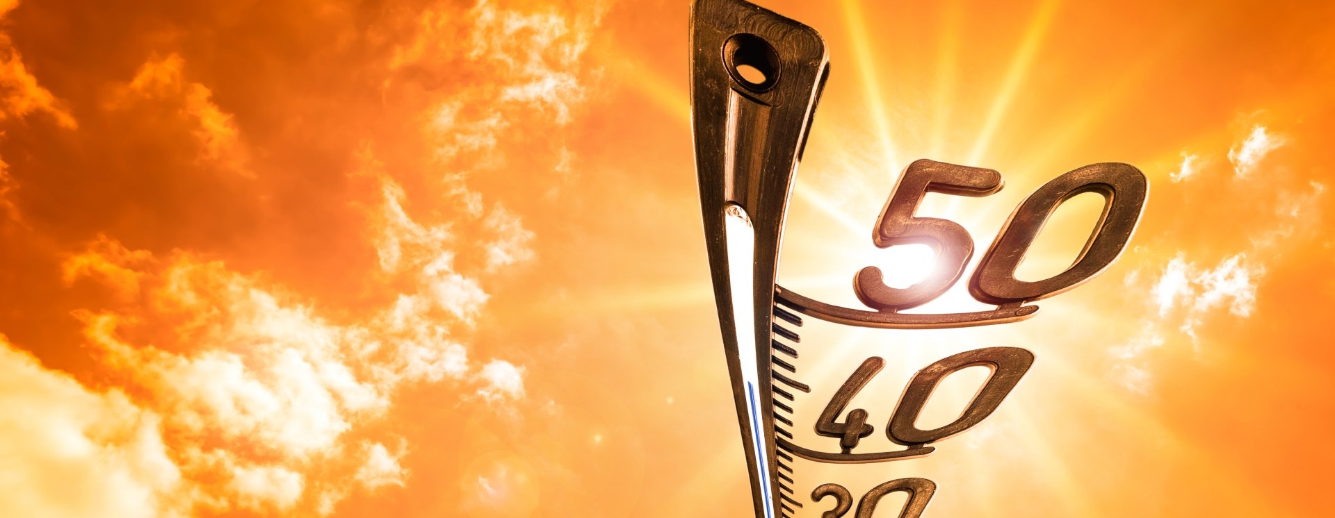 A close-up of a thermometer against a blazing orange sky, showing 50°.