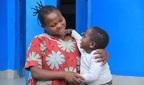 A smiling woman holds her recovered child in front of a bright blue wall. They look at each other with warmth and joy.