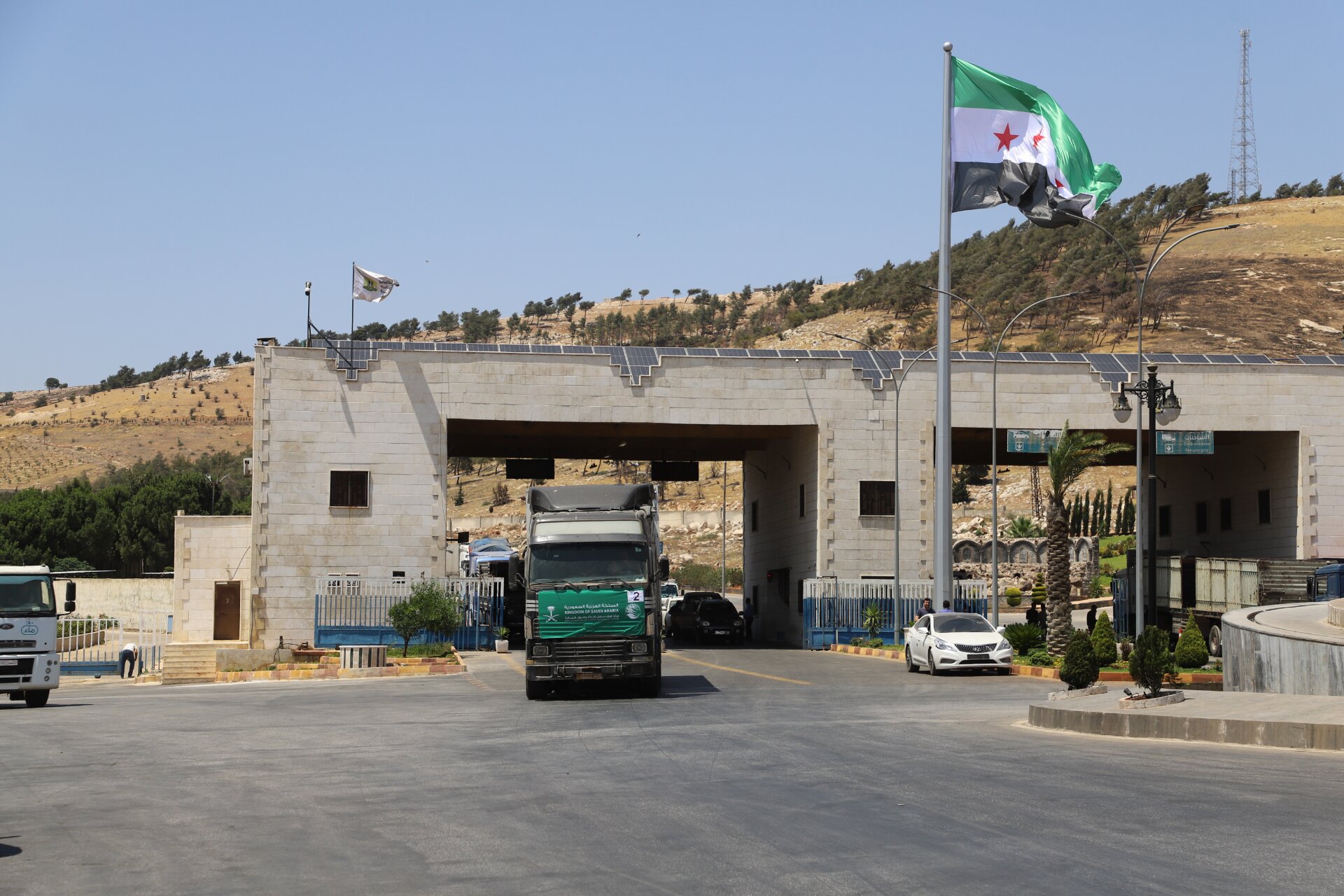 A truck is driving through a border point with a Syrian flag.