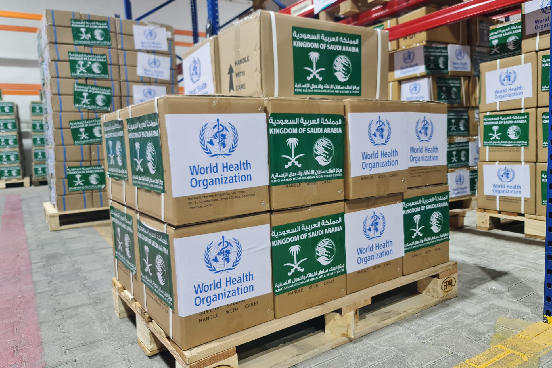 Boxes with the WHO and KSrelief logos in a warehouse.