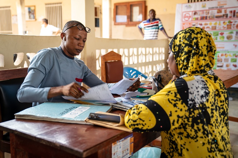 Two people sitting at a desk facing each other and looking at paperwork.