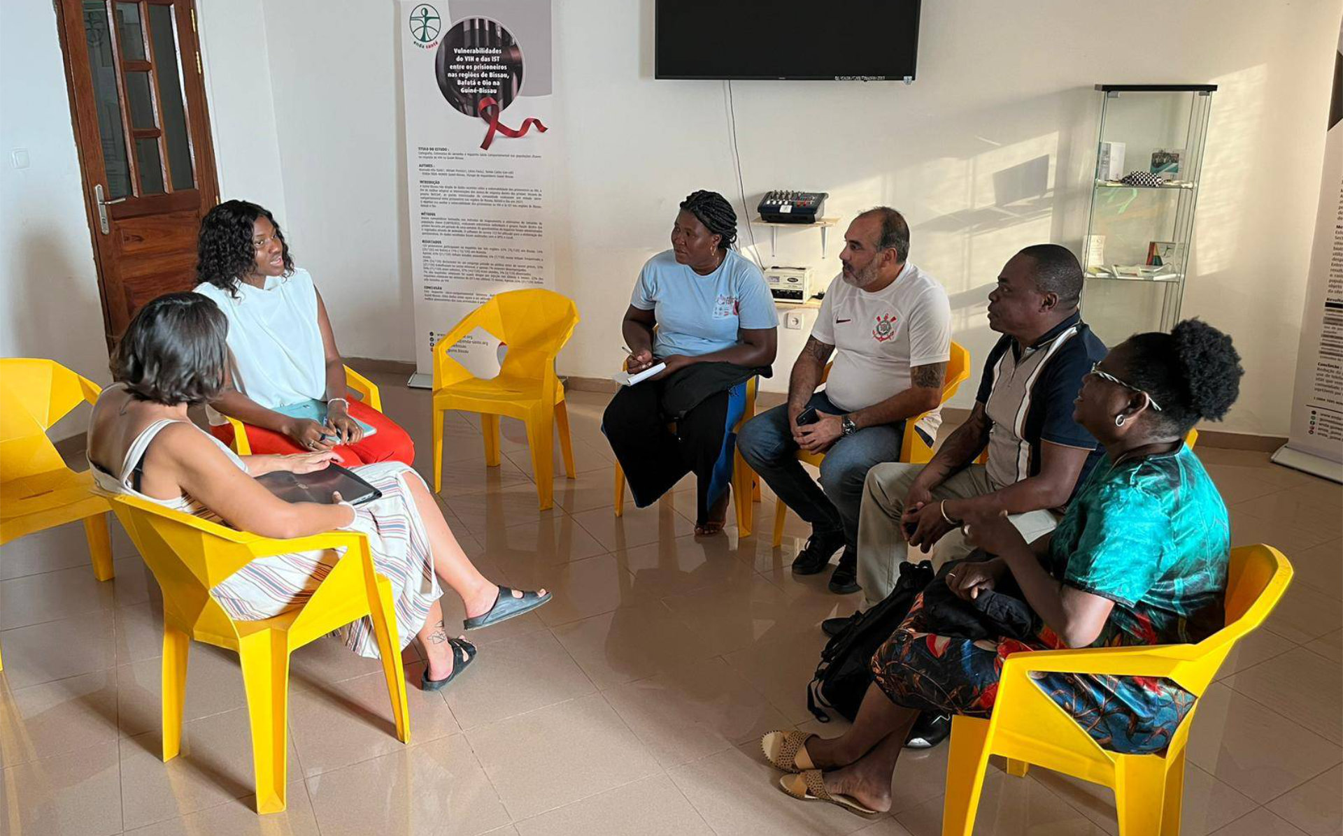 Several people sitting in chairs, participating in a discussion in a spacious indoor setting.