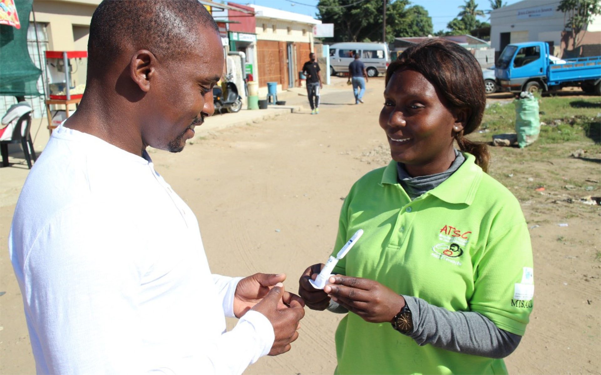 A woman with green t-shirt presents a HIV self-test kit to a man wearing a white t-shirt