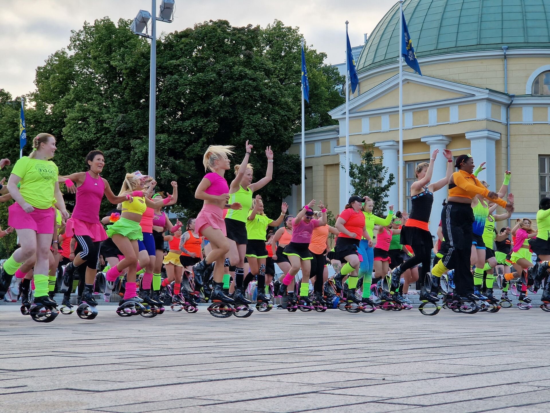 Group fitness event with rebound shoes in front of a yellow building with blue flags.