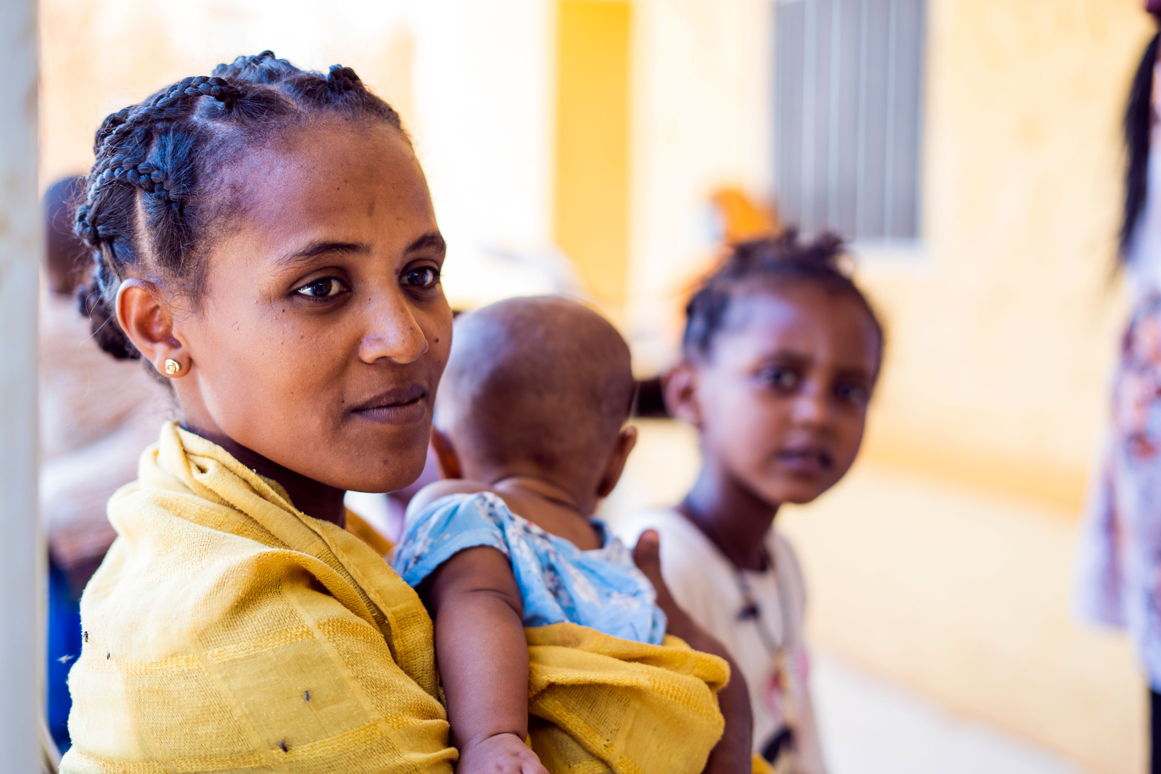A mother holding a baby and a little girl in the background