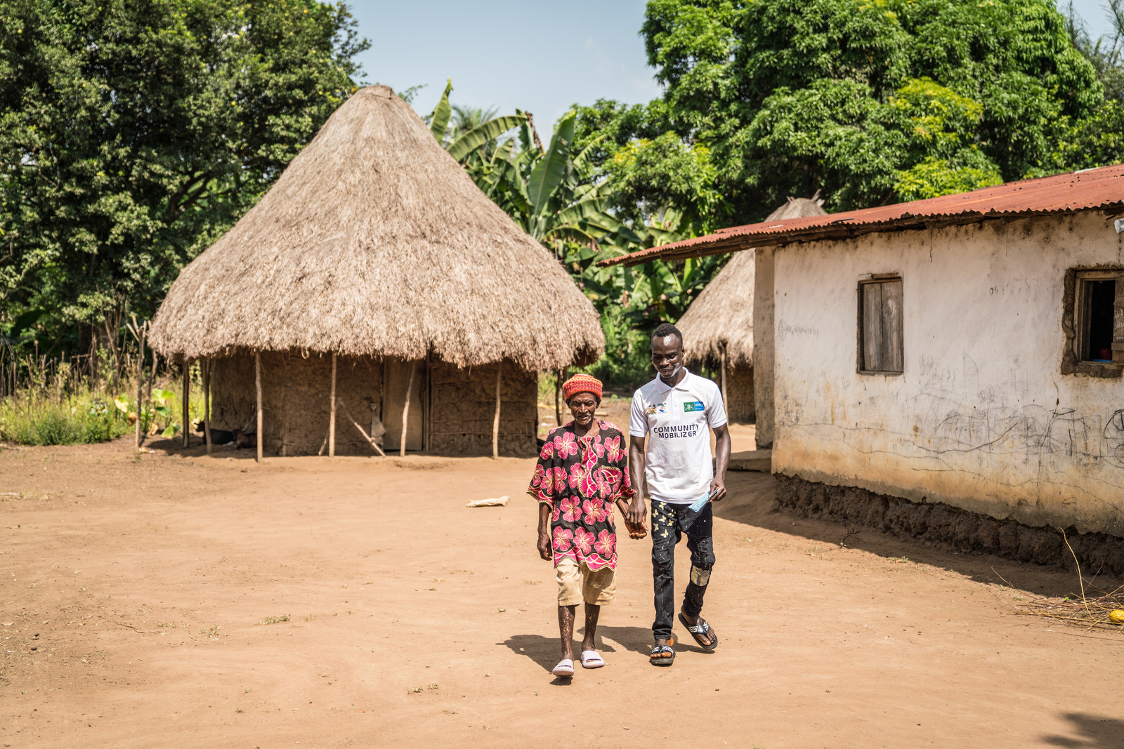 Community mobiliser Jeremiah (right) walks Amara (left) to a mobile COVID-19 vaccination clinic set up his village, Kamoi, on 8 December 2022.