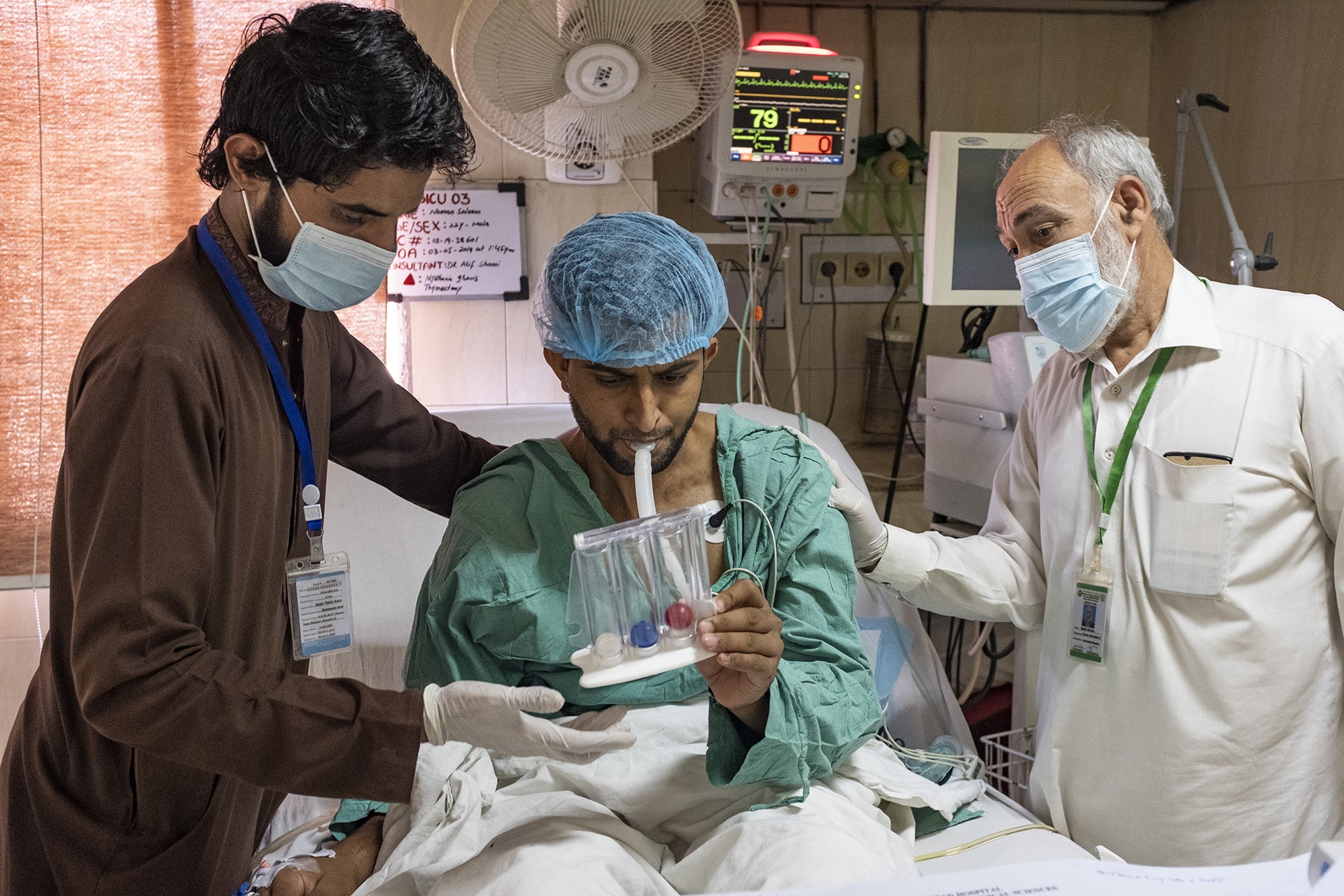 A patient on a bed doing physical rehab with 2 health workers assisting