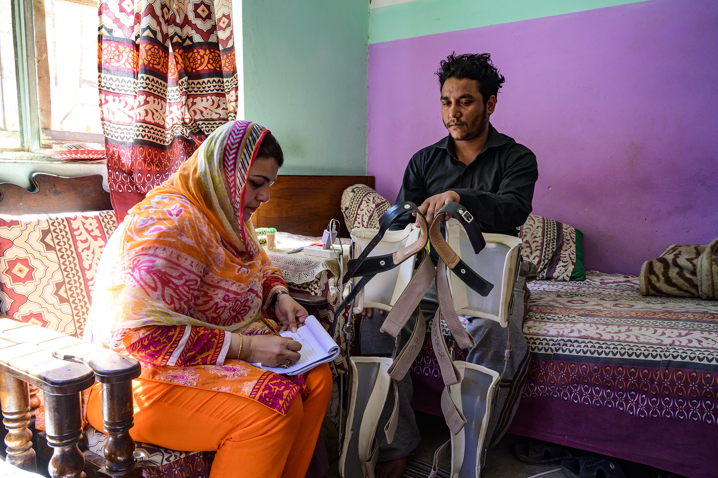 Disabled man sitting on bed while a woman is writing notes on notepad