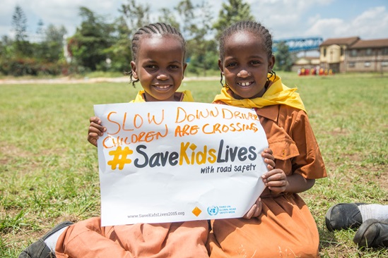 Two children holding a poster saying "slow down driver, children are crossing"
