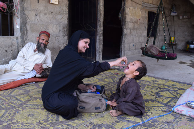 A woman gives a vaccination to a child while a man watches.