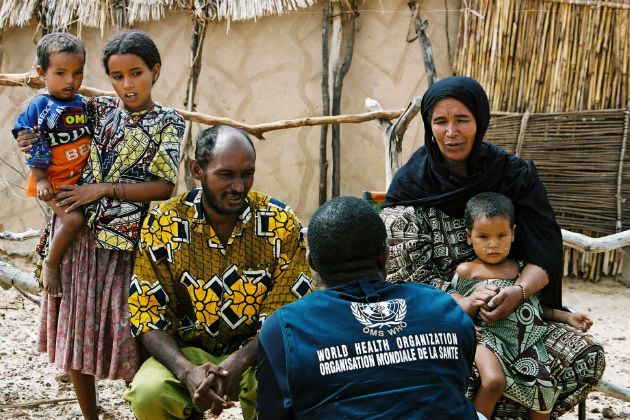 A person wearing a WHO vest talks with a family.