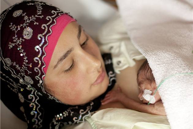 mother holds her premature baby on her chest as he is fed with IV