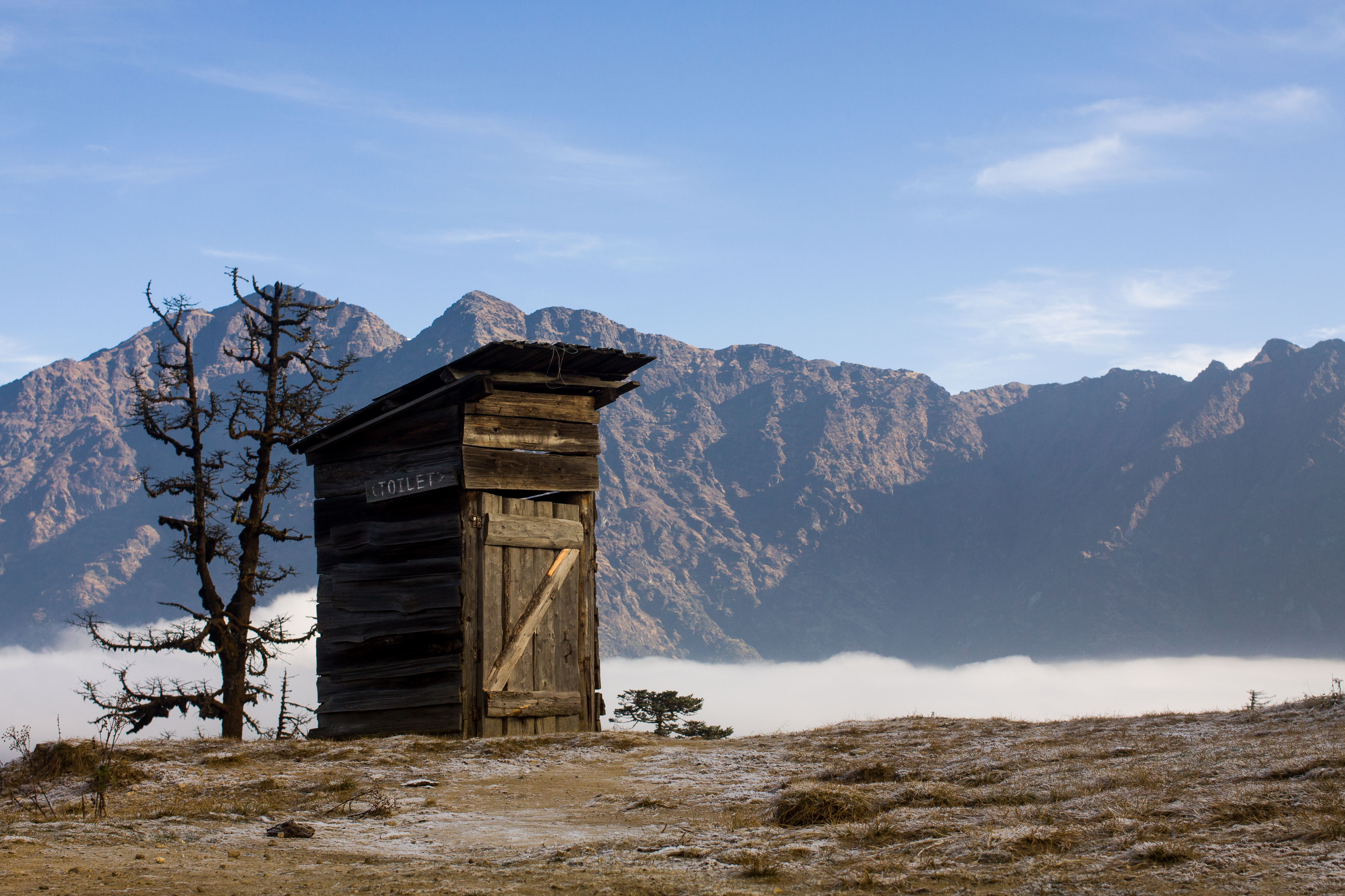 An outdoors toilet as a wooden hut in Nepal, against a mountain backdrop