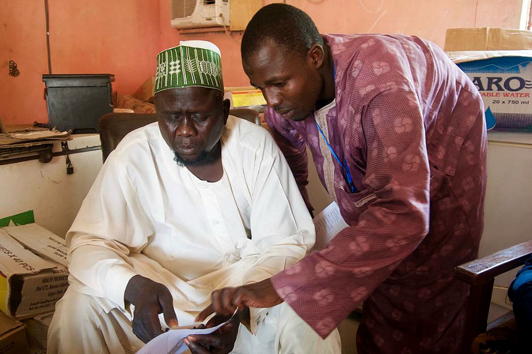 Mustapha Mohammed, Assistant Disease Surveillance Notification Officer for Monguno Local Government Area trains a colleague on the reporting of disease data via the WHO-supported EWARS system on a mobile phone. Nigeria 2016.