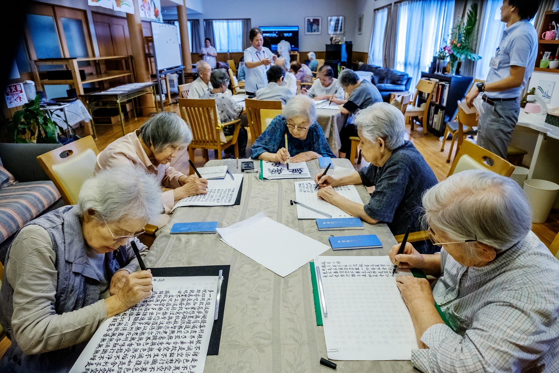 A photo depicting elderly persons doing calligraphy and Shakyo