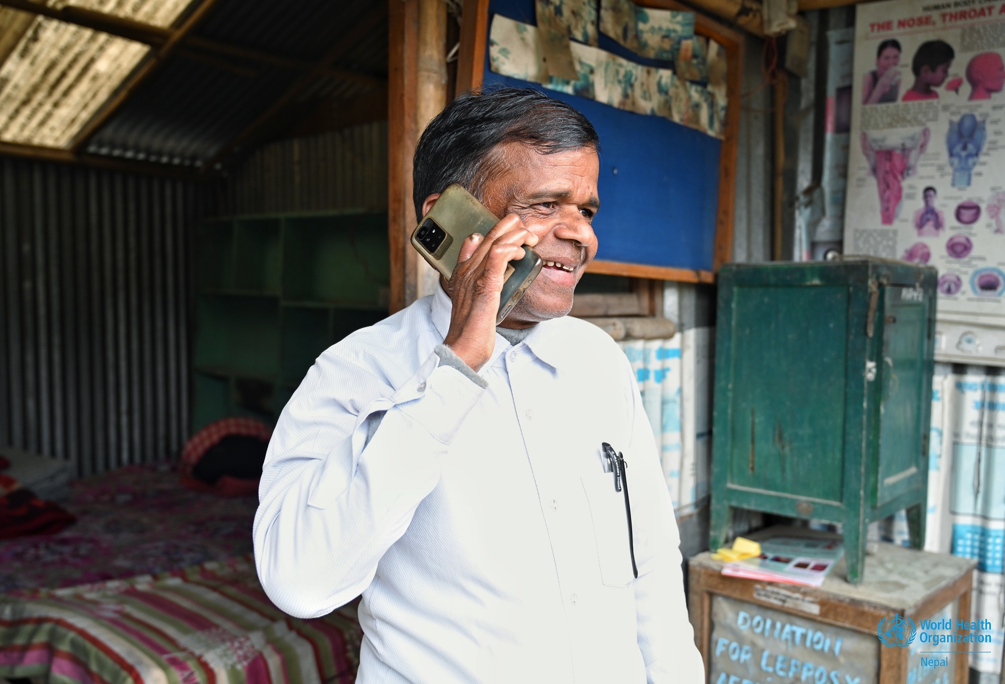 A photo of Basudev Yadav, an individual cured of leprosy, outside his office and holding a smartphone in Bagmati Province, Nepal
