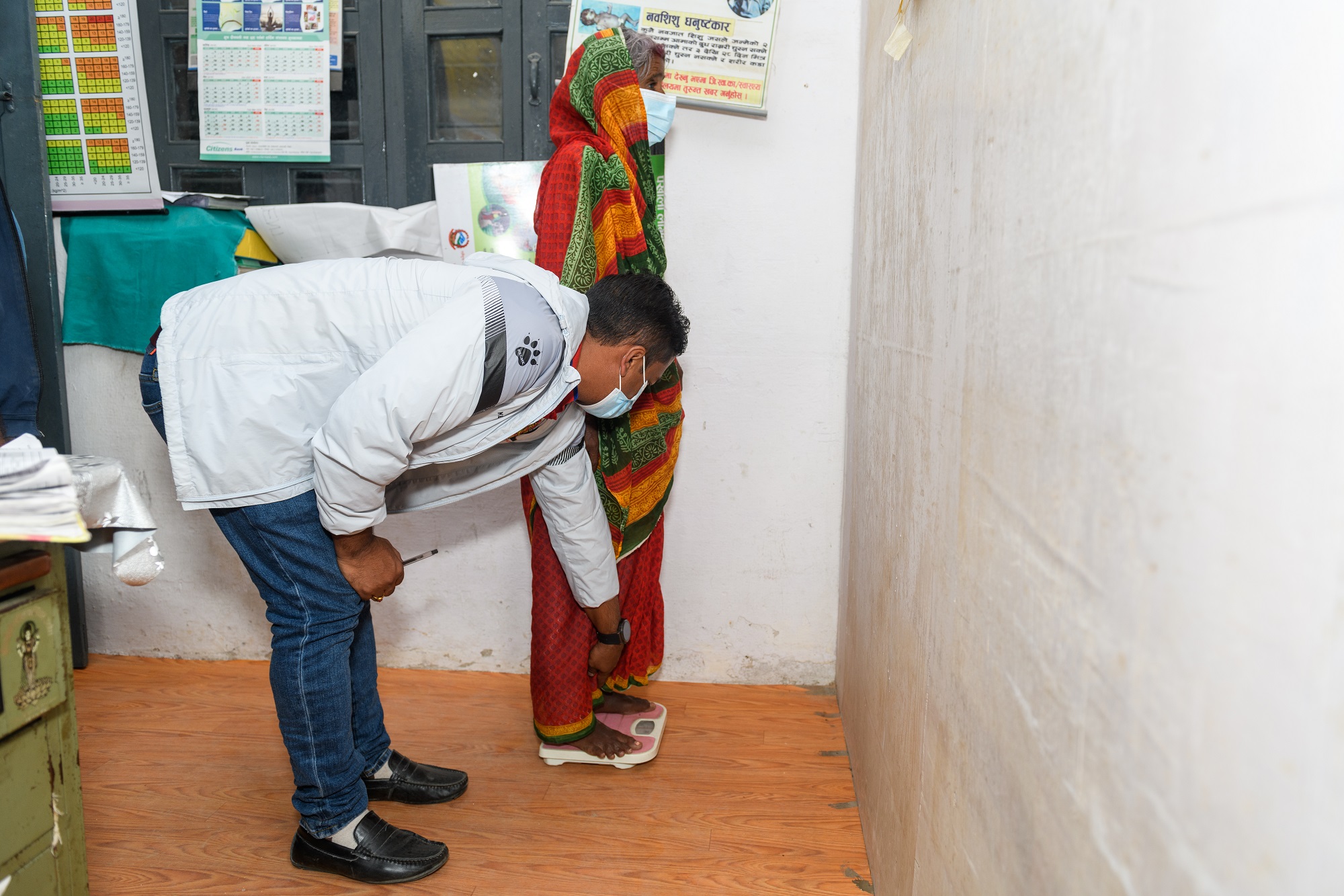 A drug-resistant tuberculosis (TB) patient measuring her weight, with the support of healthcare worker, at a TB health center in Bagmati Province, Nepal