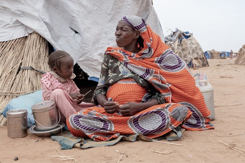 A mother sitting with her daughter in front of their shelter.