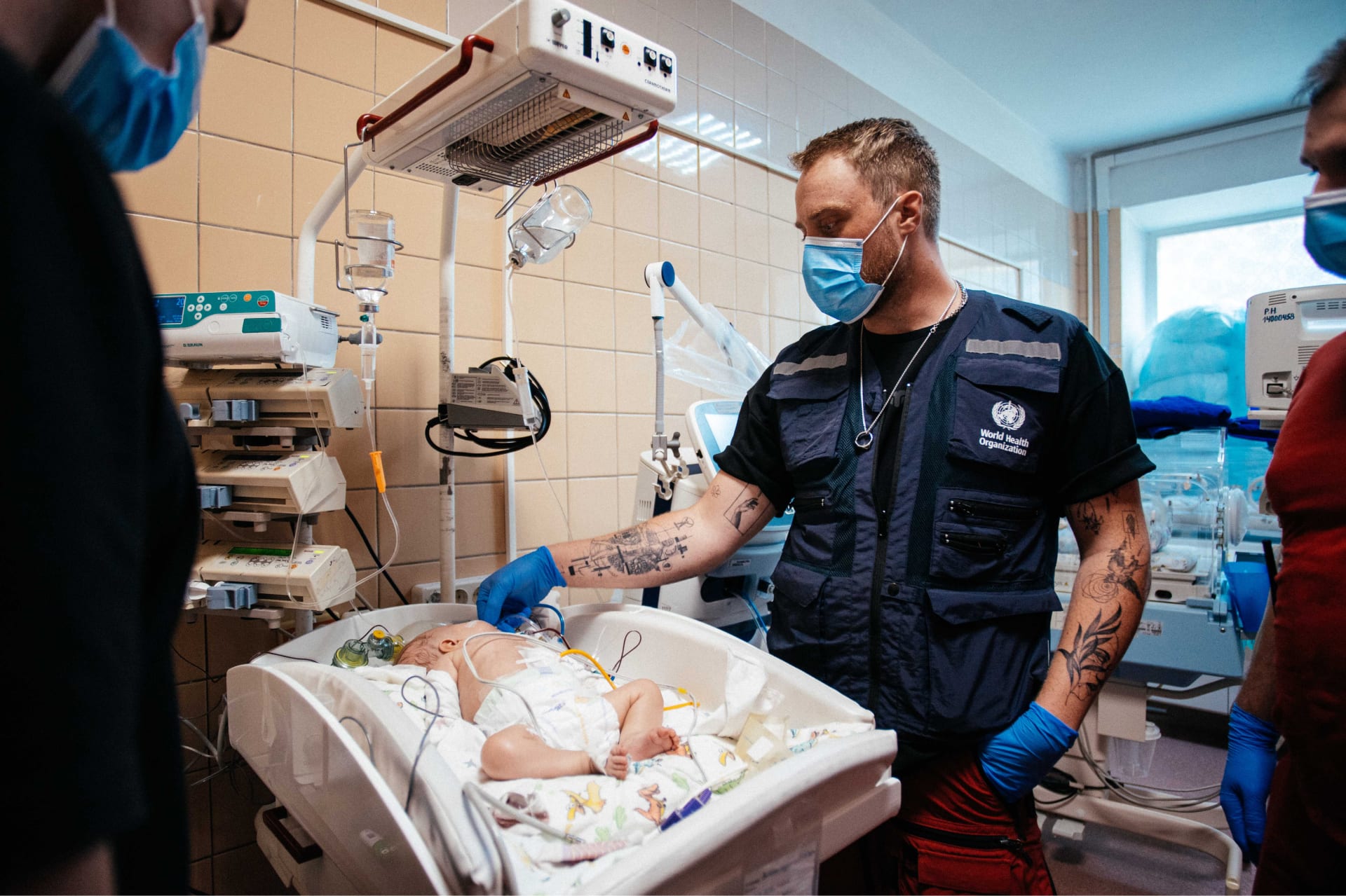 A consultant wearing a WHO vest examining a 4-month-old child in a hospital.