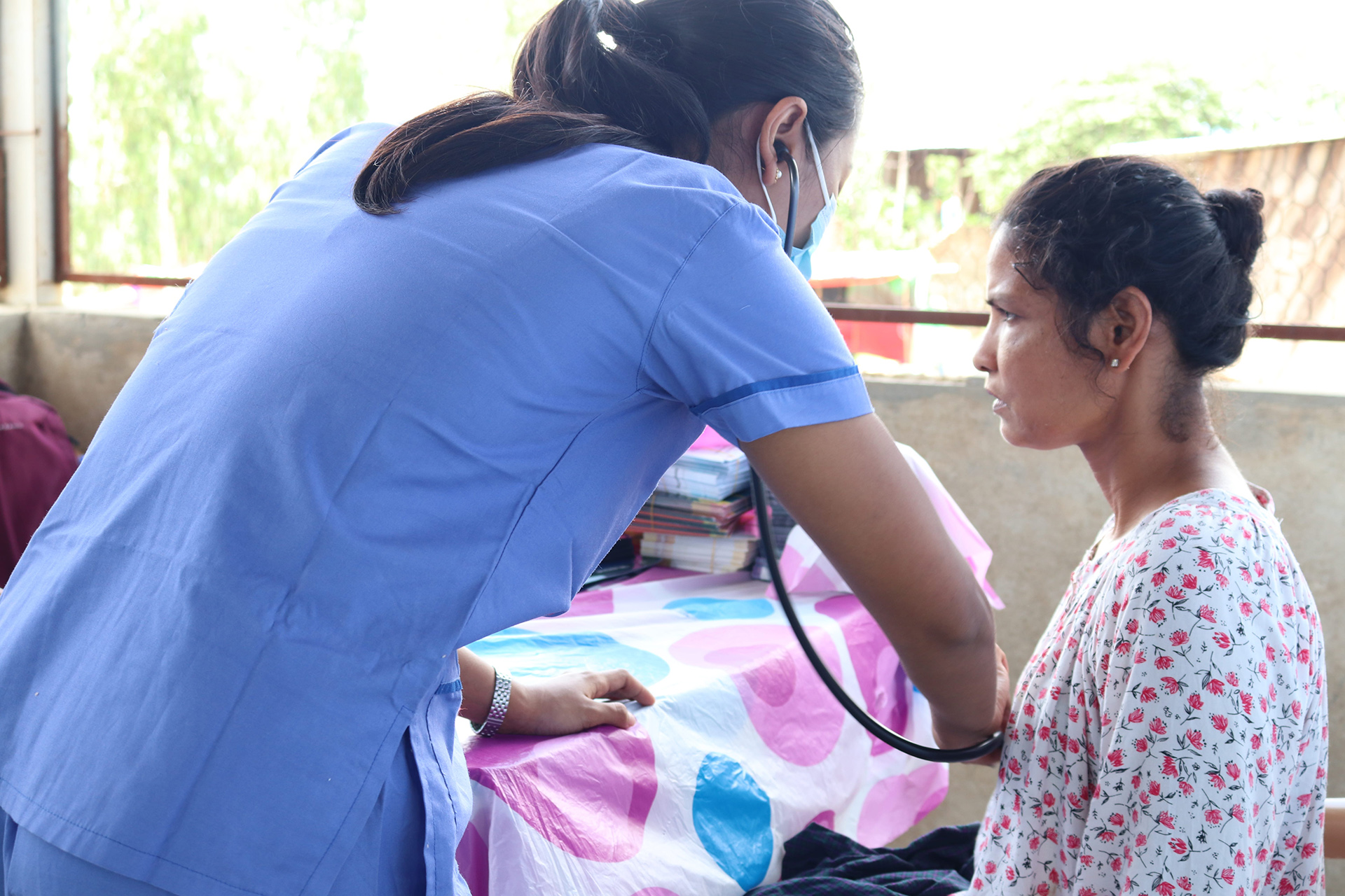 A nurse listens to a seated woman’s chest with a stethoscope in a clinic.