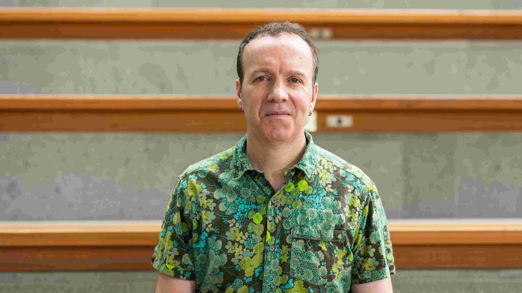 Photo of a man wearing a short-sleeved shirt in green tones.